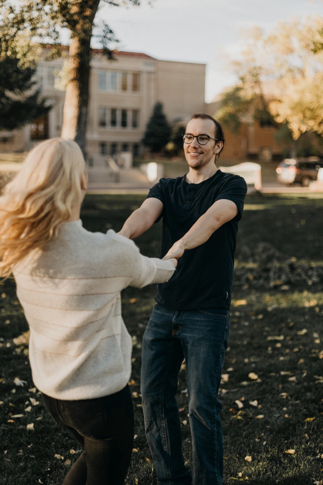 Couple spinning and laughing hand in hand on a grassy lawn in autumn light