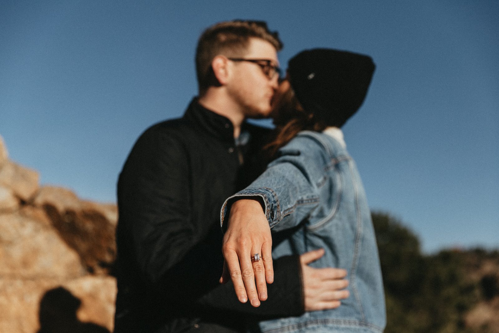 Couple kissing against a blue sky with a ring visible on her hand