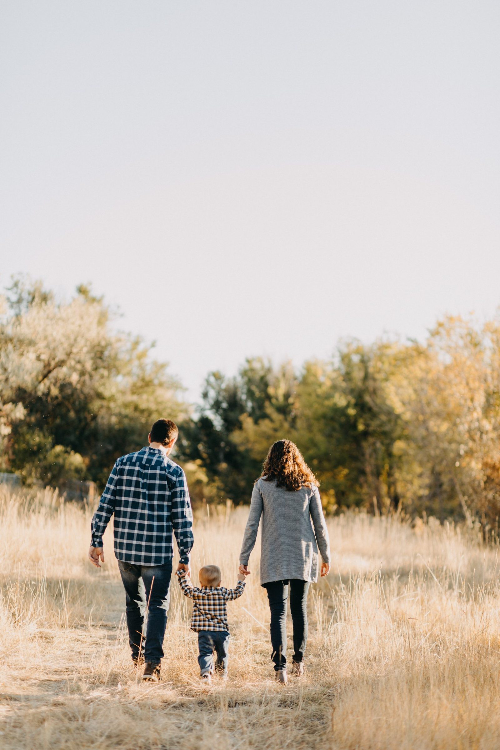 Mom, dad and toddler holding hands as they walk away through a golden autumn field