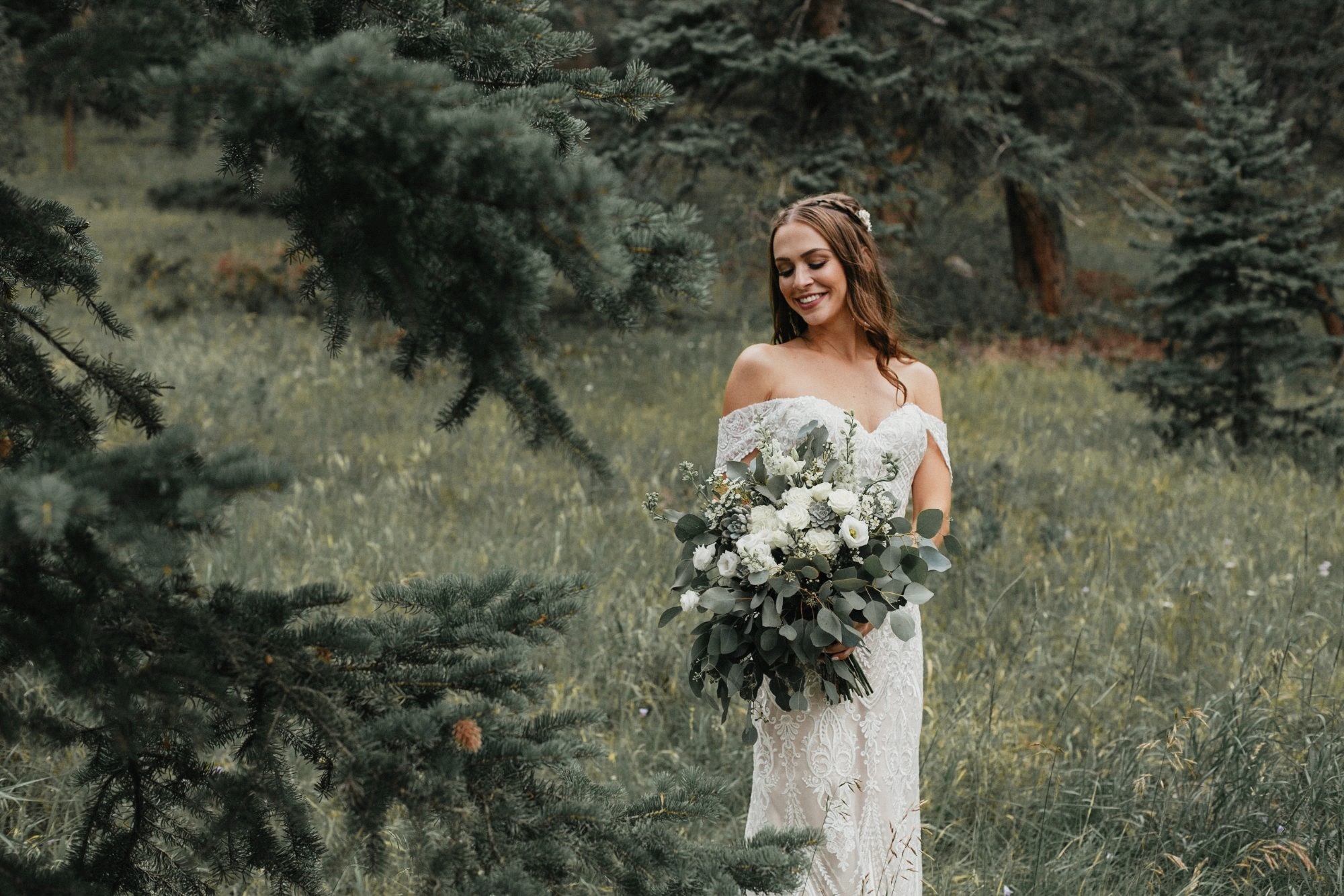 Bride holding a white bouquet standing in a green mountain meadow