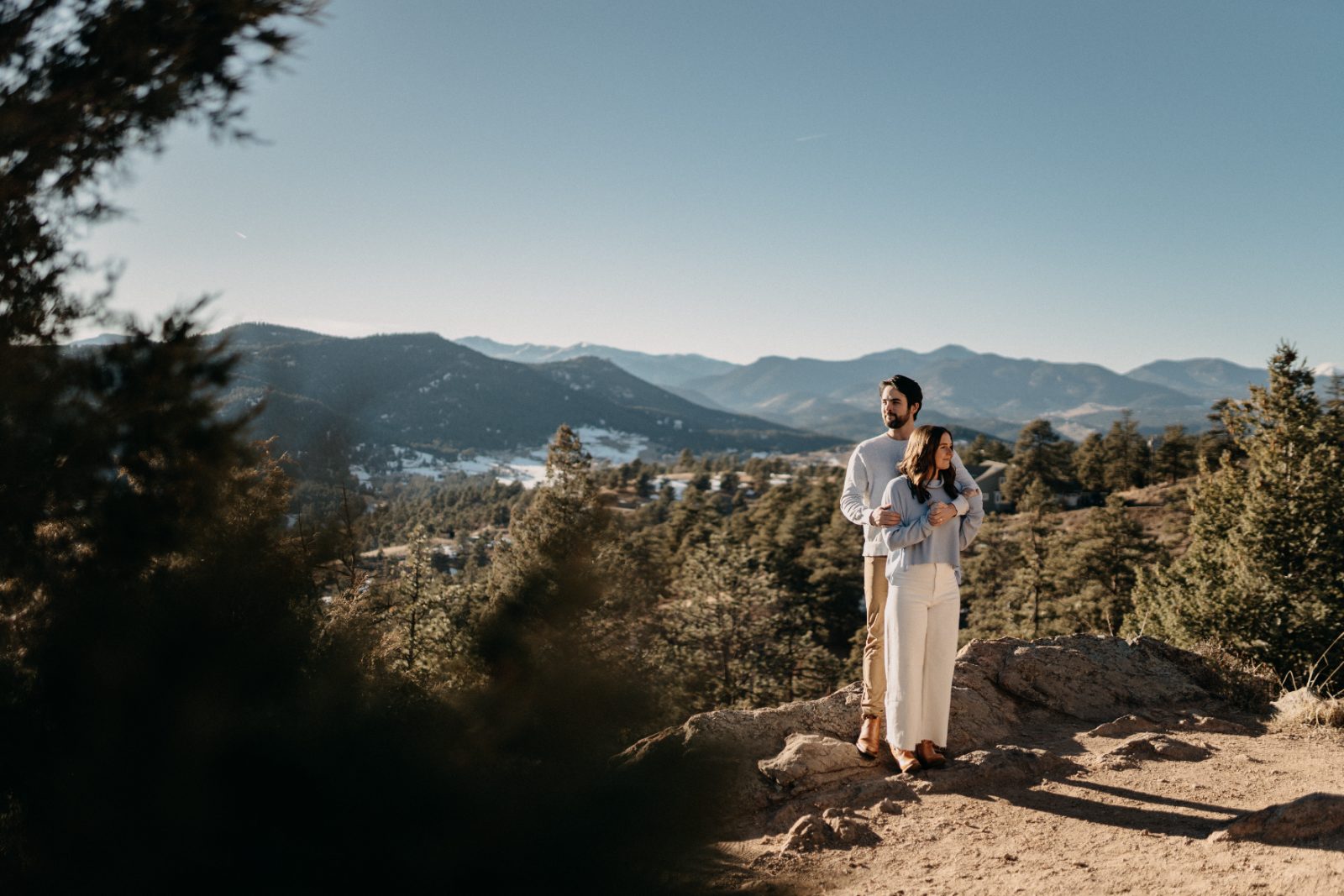 Couple standing together on a rocky overlook with Colorado mountains stretching behind them