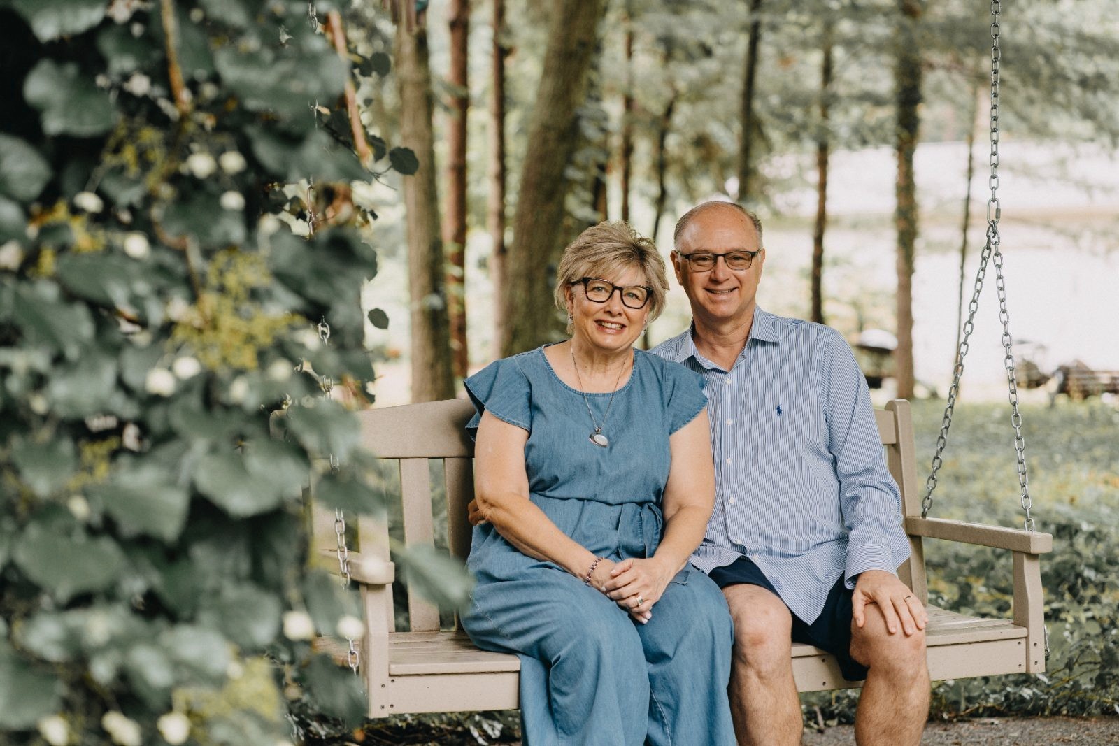 Older couple sitting on a porch swing surrounded by trees for a family portrait