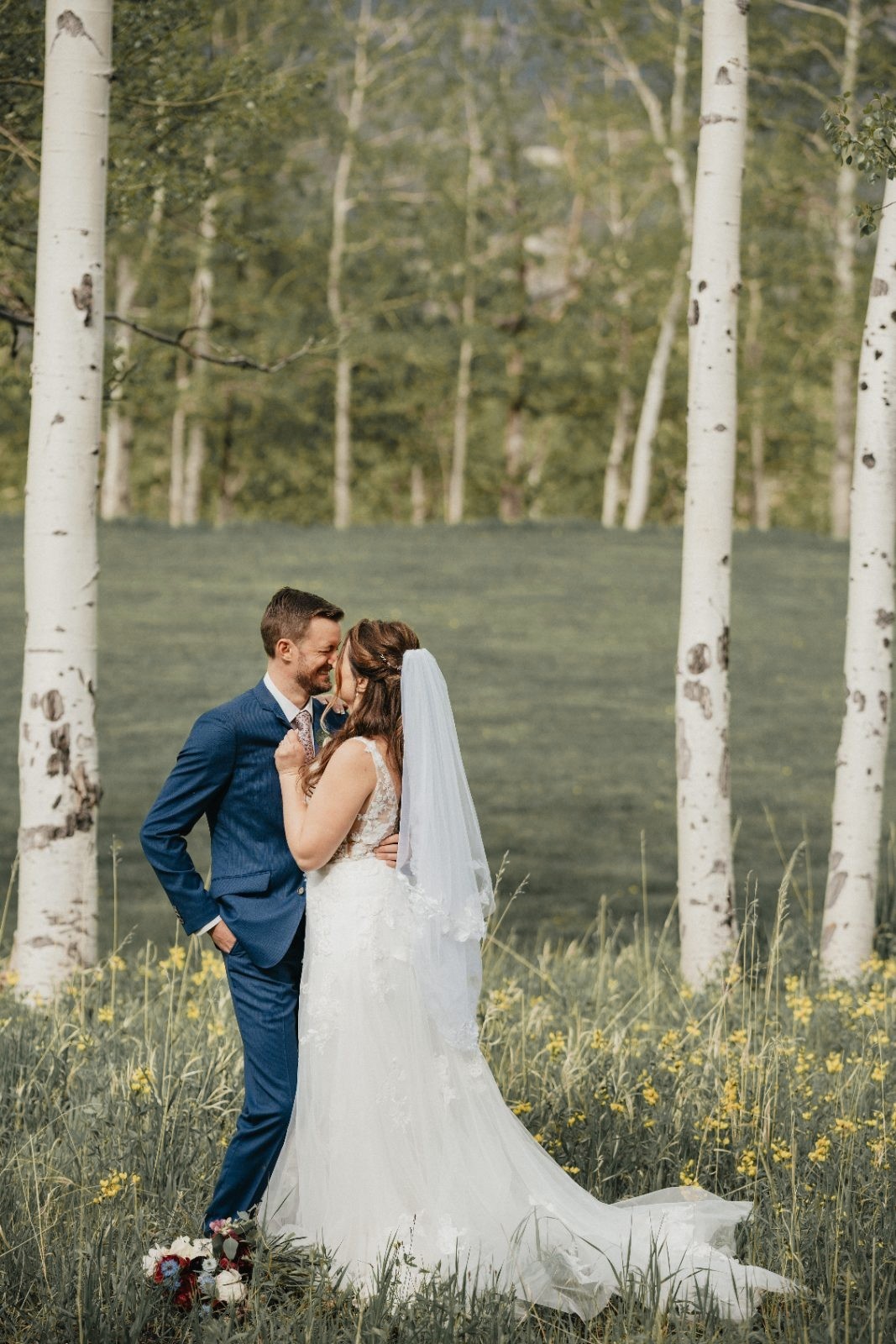 Bride and groom embracing in a field of wildflowers among white aspen trees