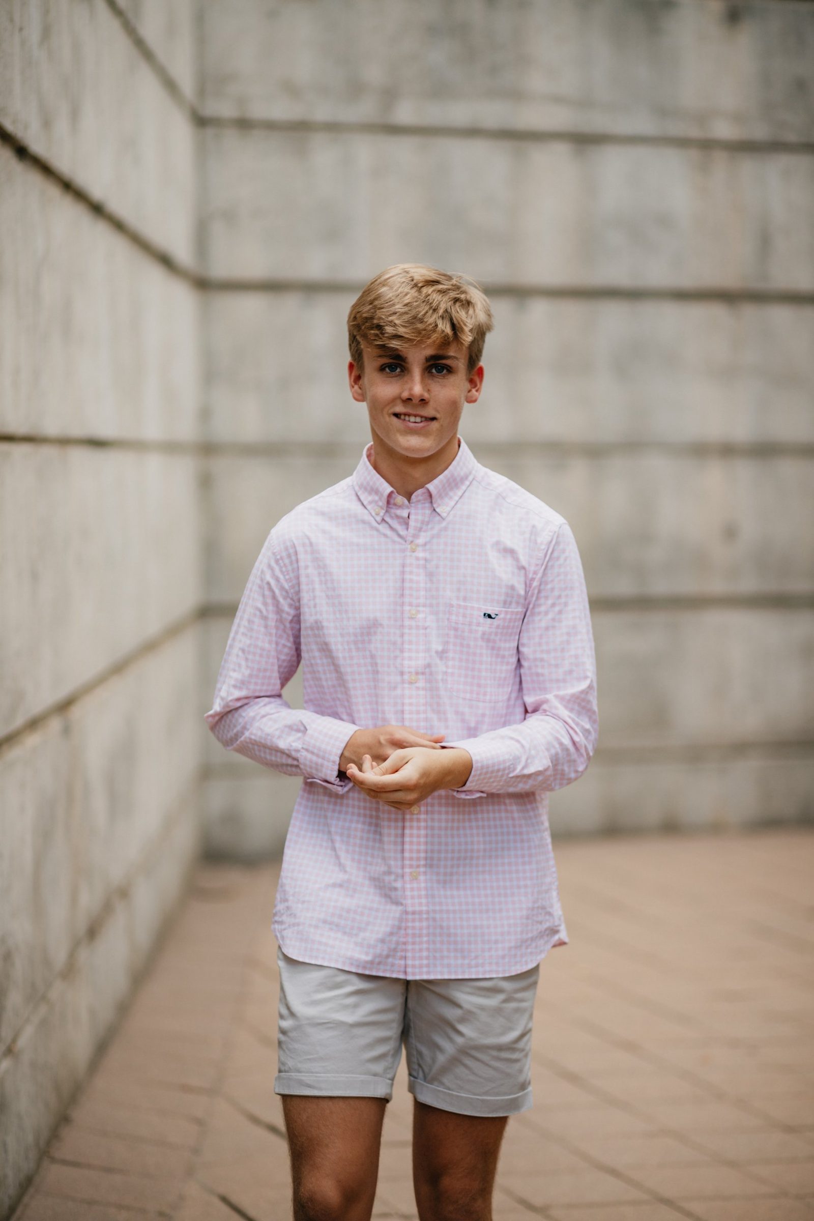 Senior in a pink gingham button-down standing in a concrete corridor