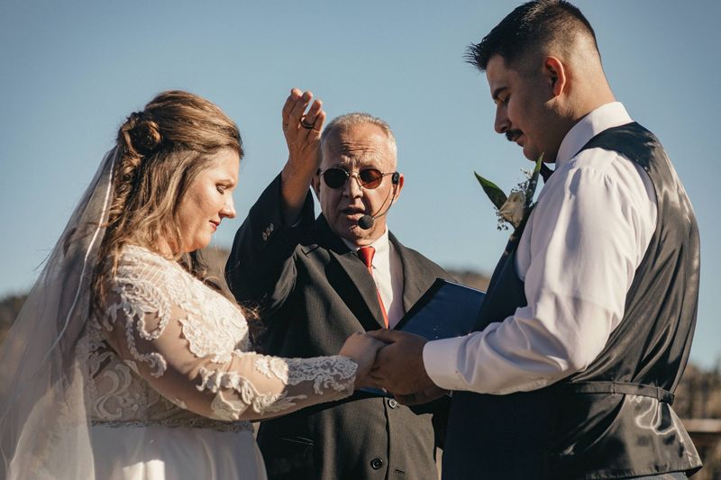 Bride and groom exchange rings during an outdoor ceremony as the officiant looks on