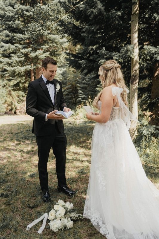 Bride and groom read handwritten vows to each other in a sunlit evergreen forest