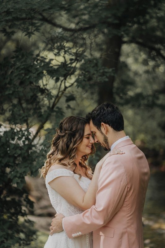 Bride and groom touch foreheads in a quiet moment among green trees