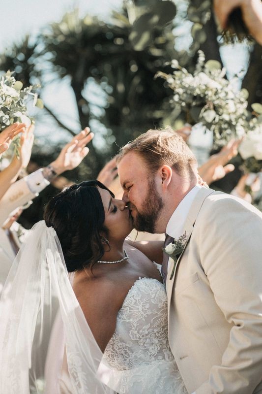 Bride and groom kiss as guests raise their hands to cheer after the ceremony