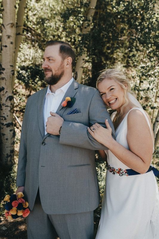 Groom in a gray suit with his smiling bride tucked under his arm among aspen trees