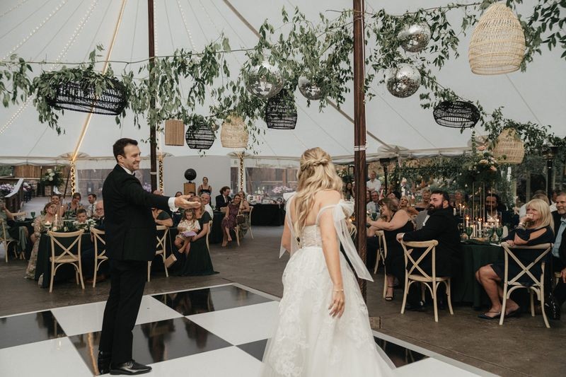 Bride and groom share a dance under a tented reception with hanging greenery and a checkerboard floor