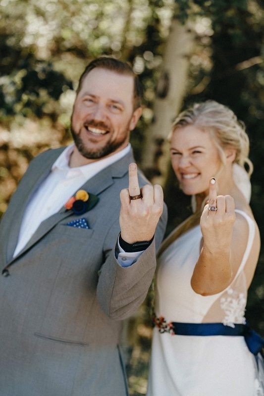 Bride and groom smile at the camera and show off their wedding rings