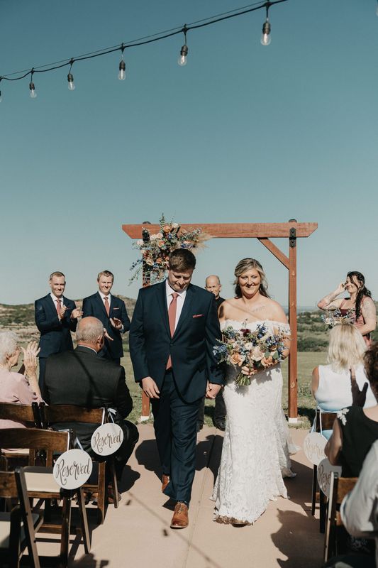 Newlyweds walk up the aisle after the ceremony under string lights as guests applaud