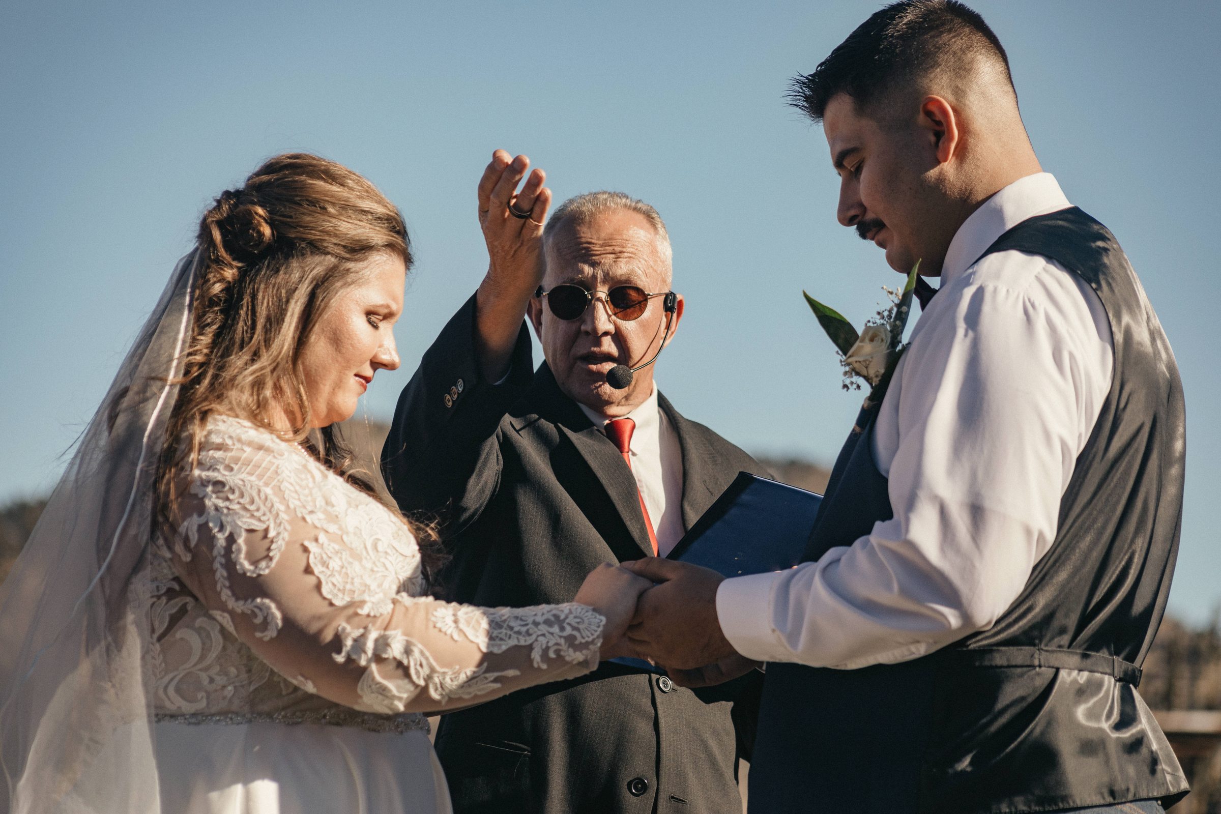 Bride and groom exchange rings during an outdoor ceremony as the officiant looks on