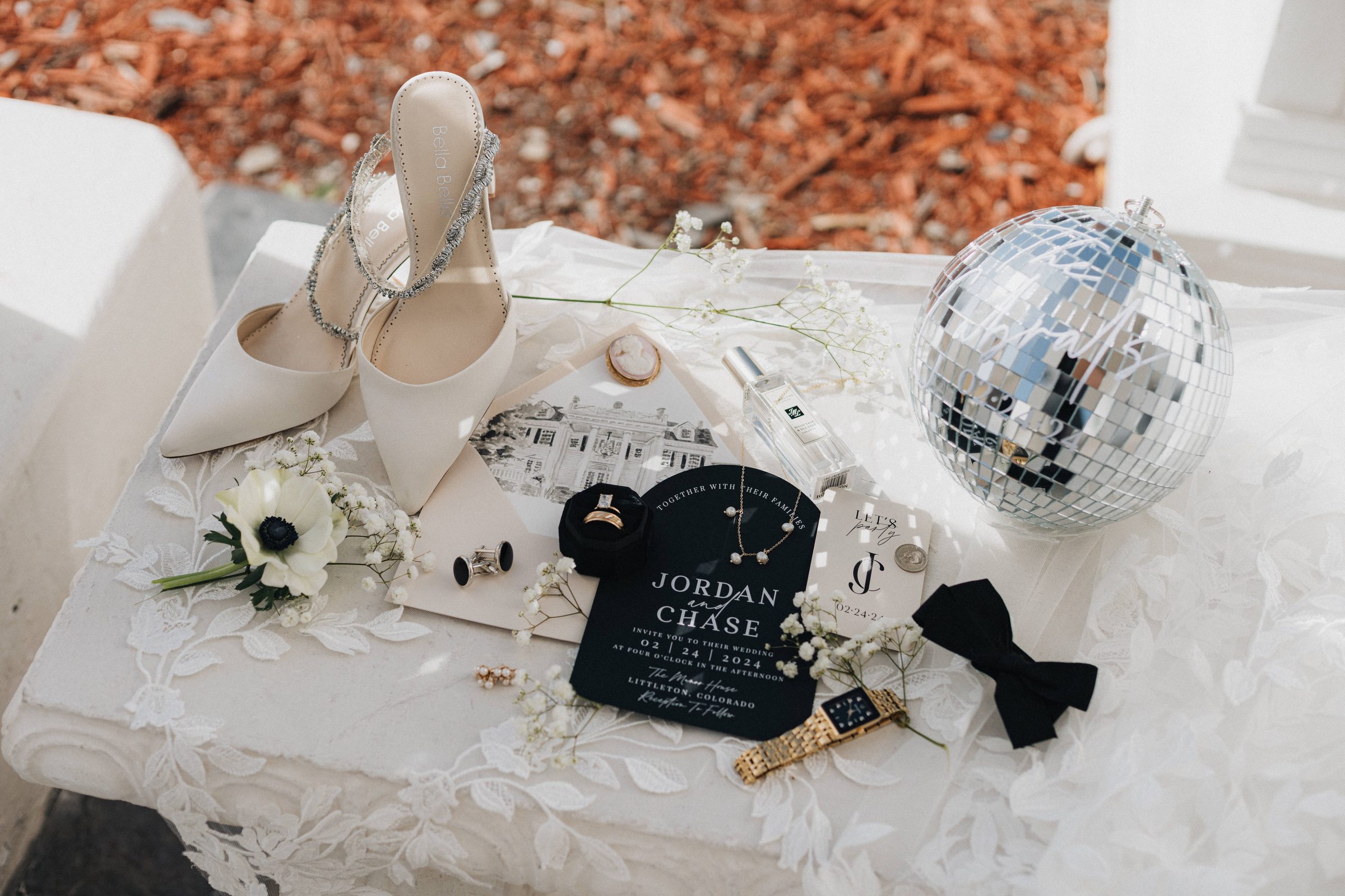 Wedding day details flat lay with heels, invitation, rings, bow tie and a mirror disco ball