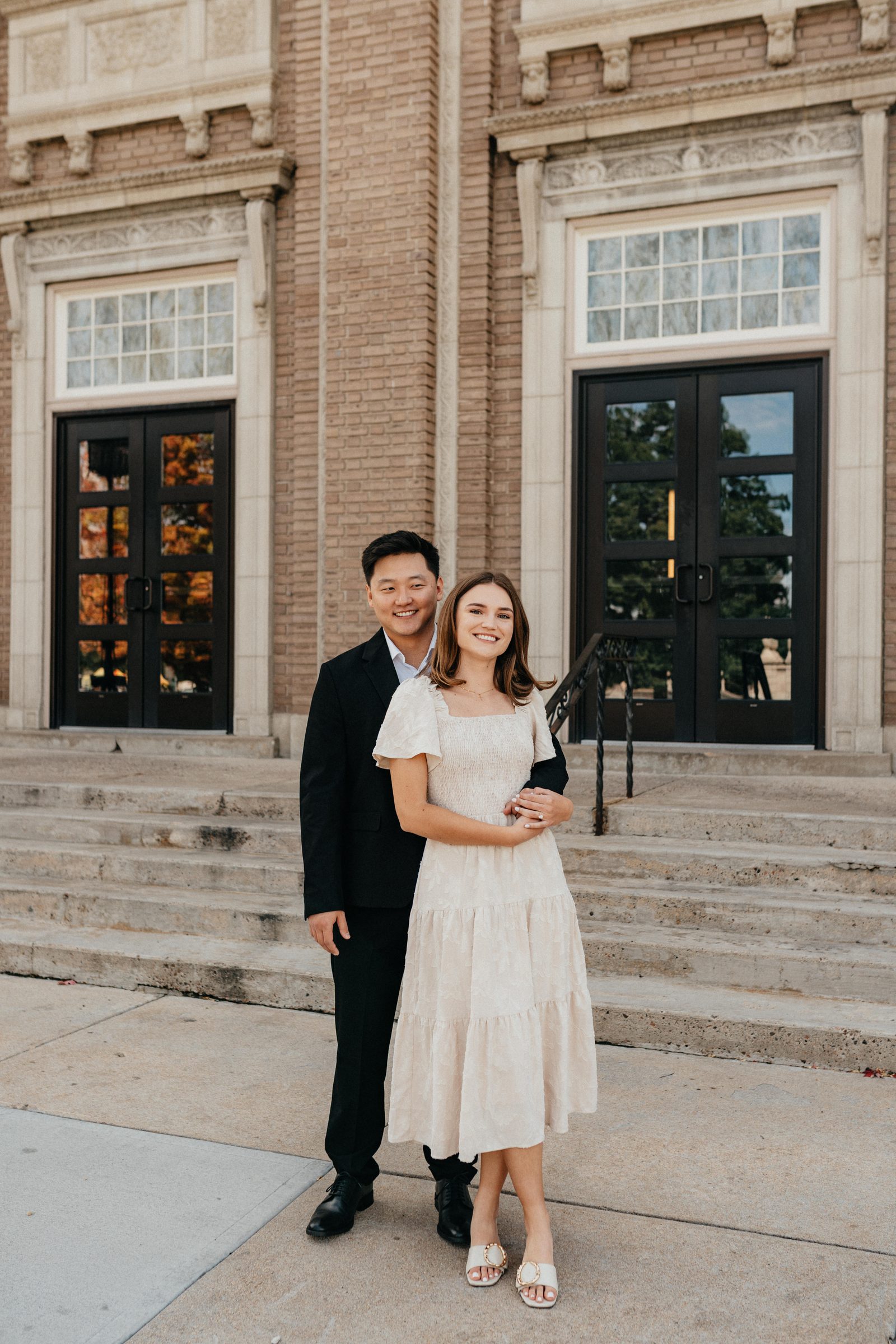 Couple embracing on the steps of a historic brick building in front of tall black doors