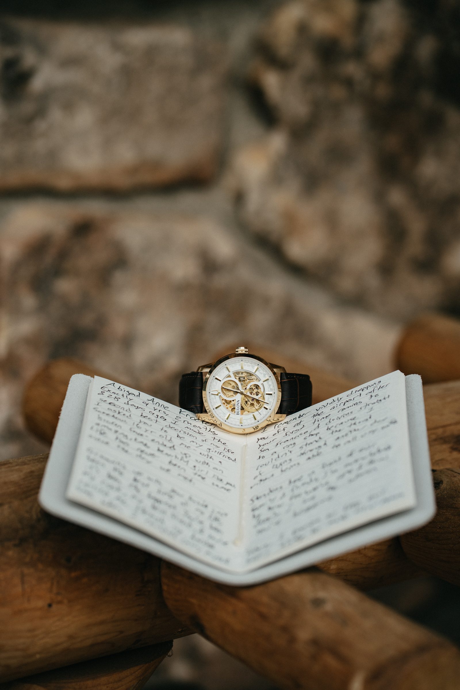 Vintage watch resting on an open handwritten vow book atop a log