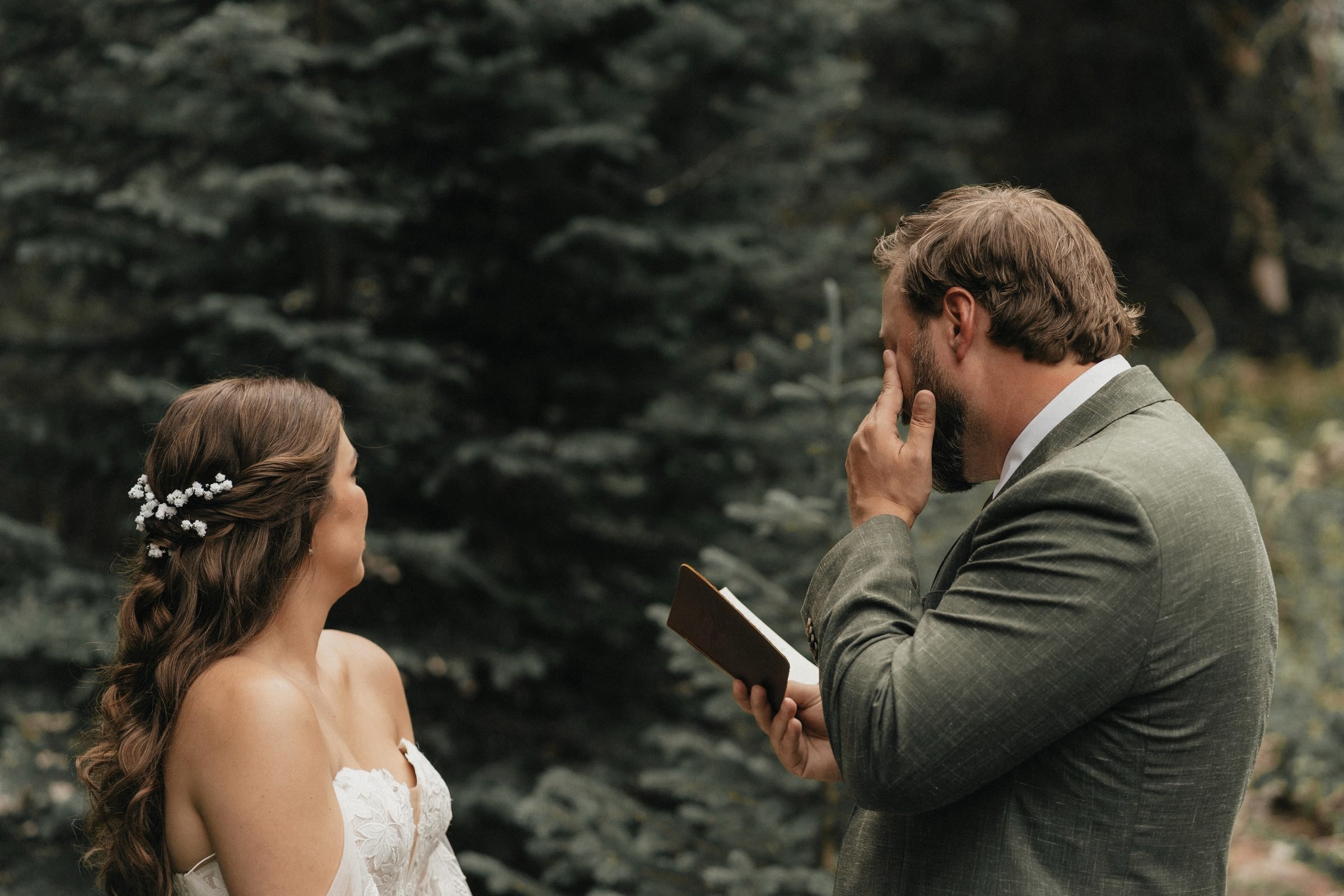 Groom wipes away tears while reading private vows to his bride during a first look in the pine forest