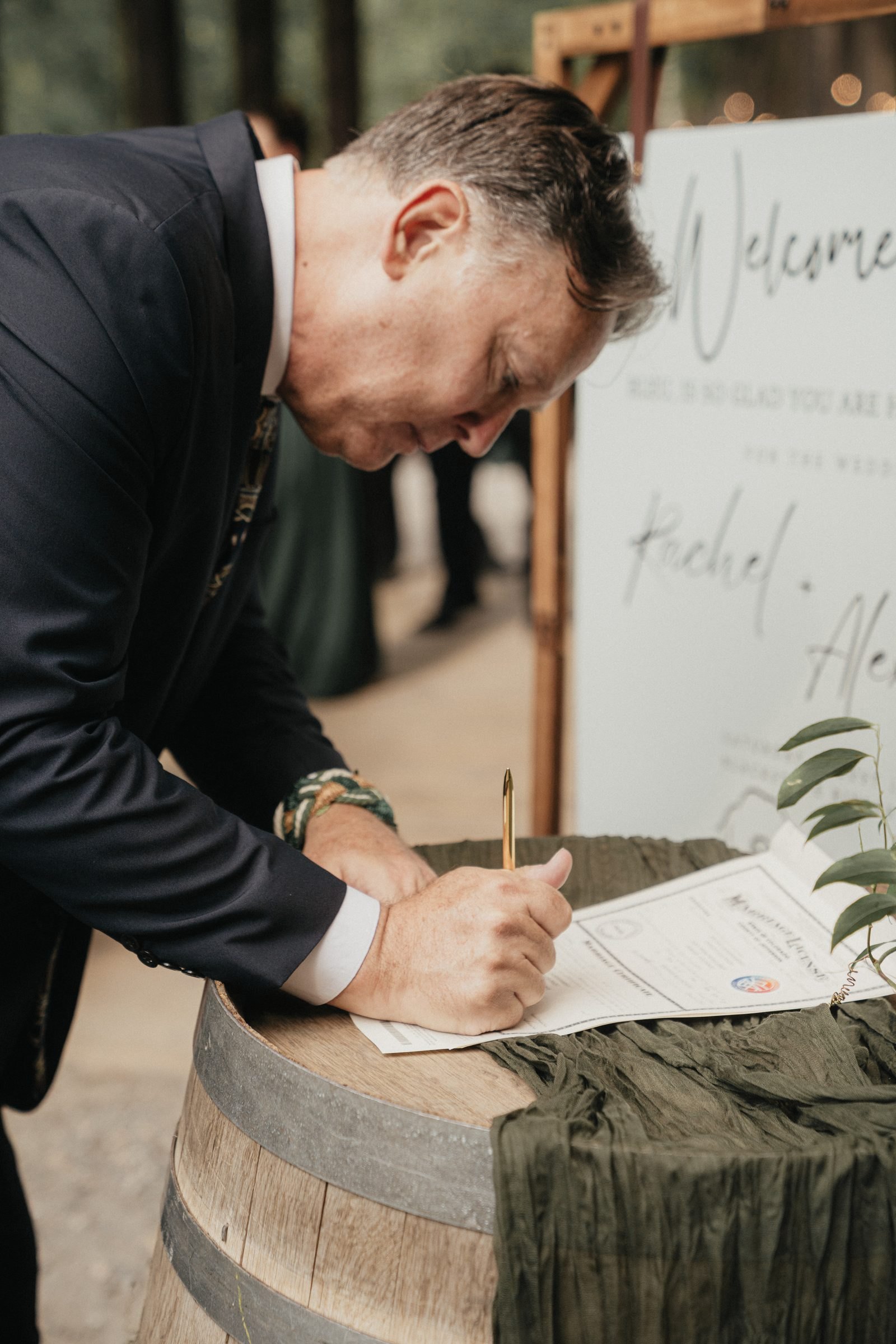 Officiant signs the marriage license on a wine barrel beside a welcome sign