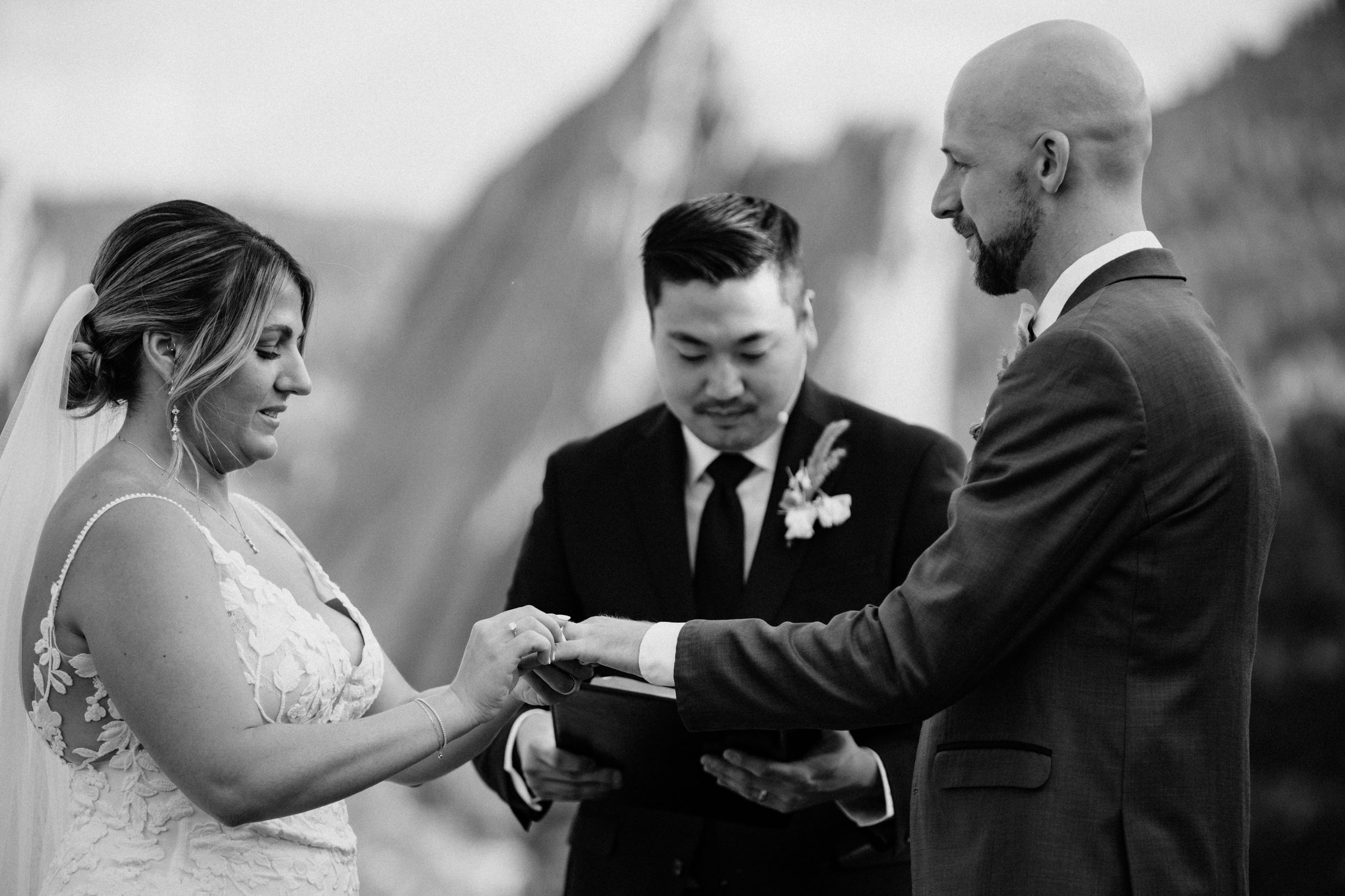 Black and white photo of the bride and groom exchanging rings with rock formations behind them