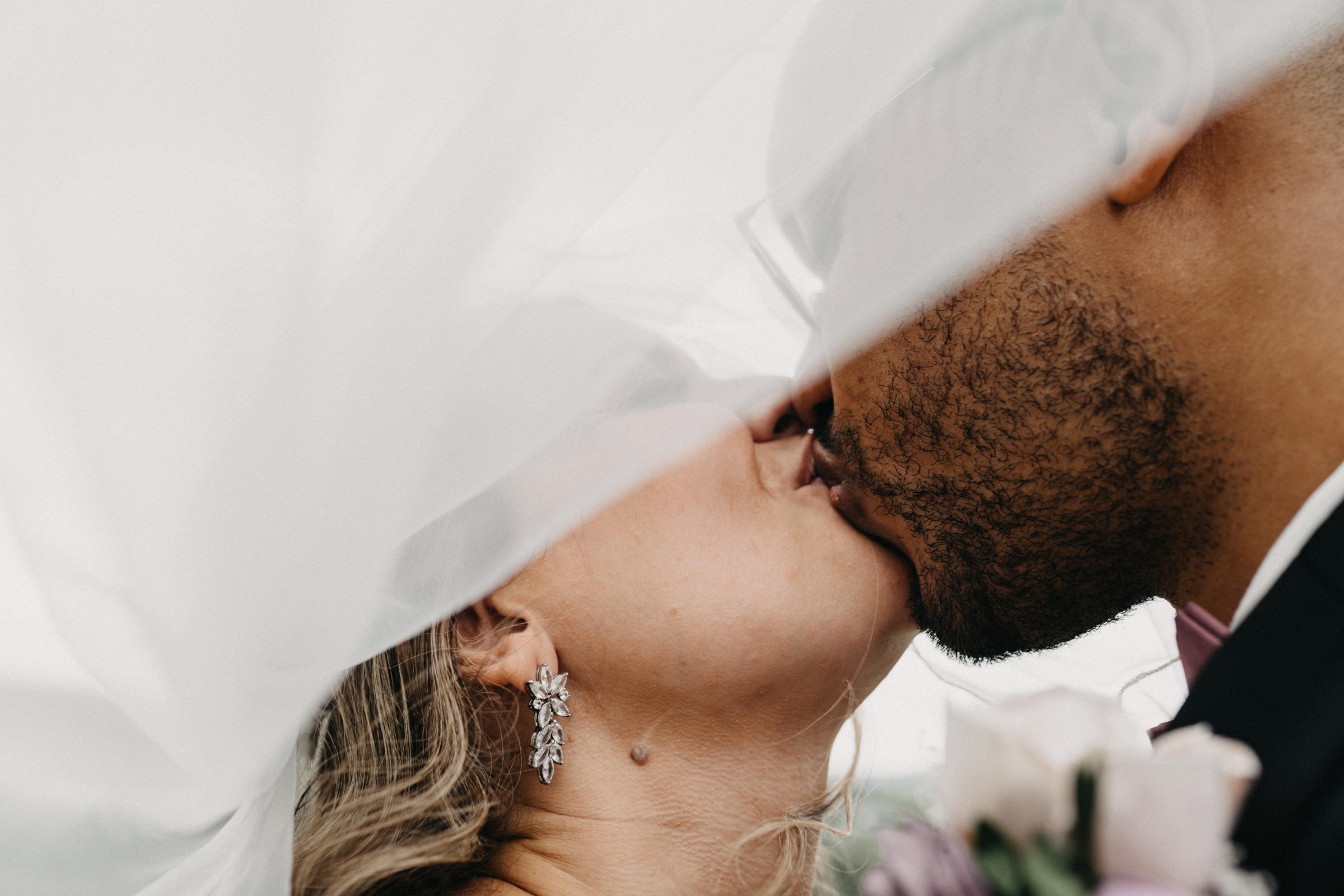 Close-up of a bride and groom kissing beneath the bride's sheer veil