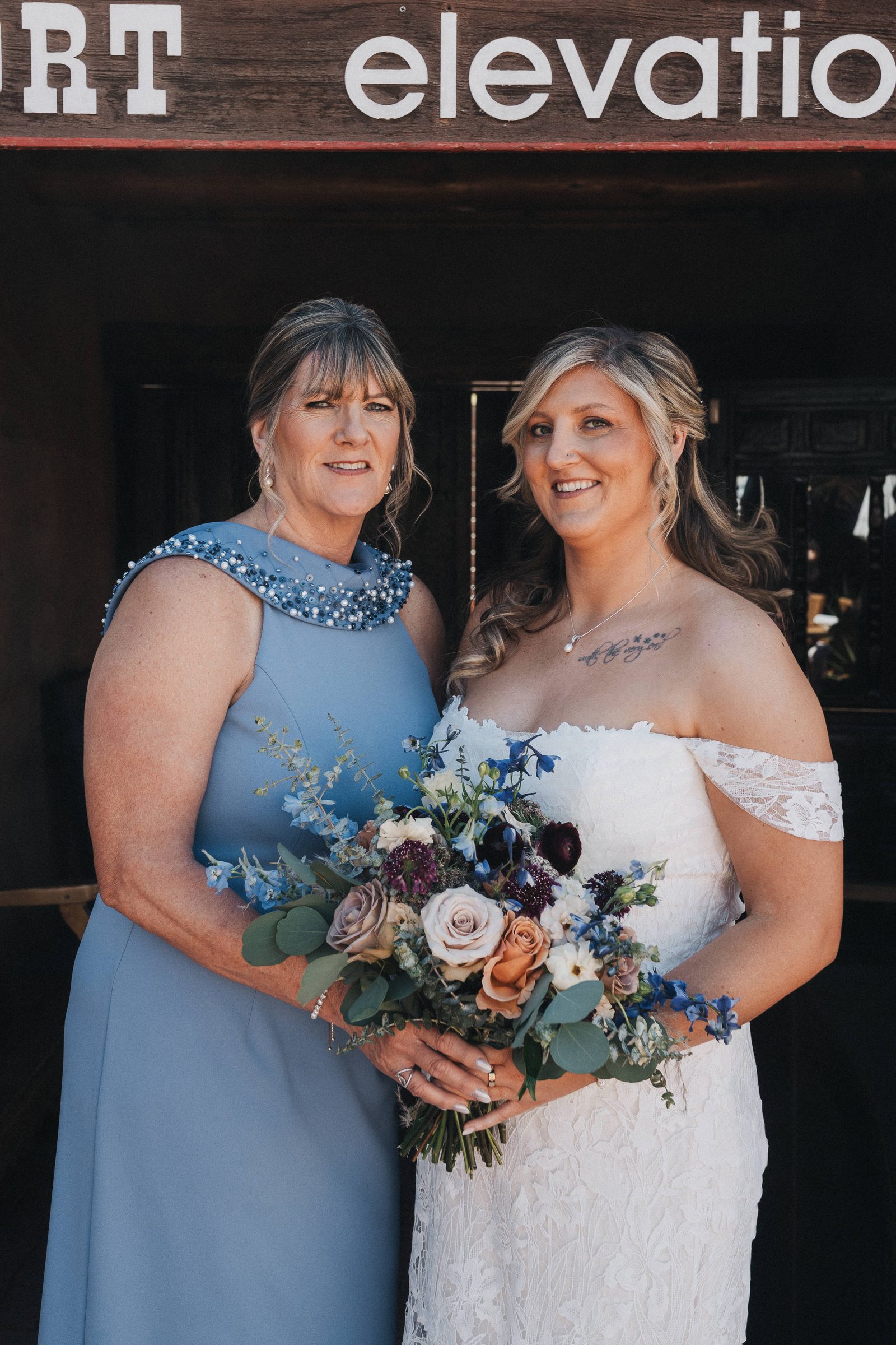 Bride with her mother, who is wearing a blue dress, holding a colorful bouquet