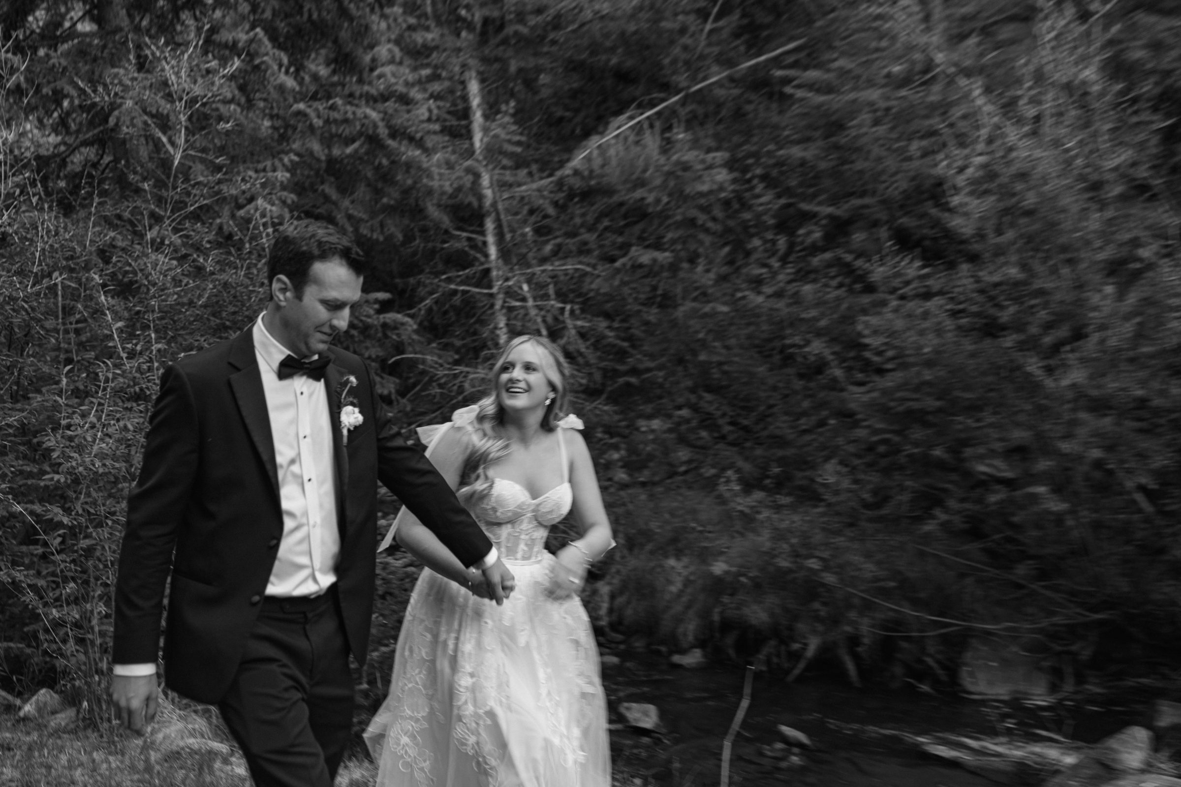 Black and white photo of a couple walking hand in hand along a forest creek