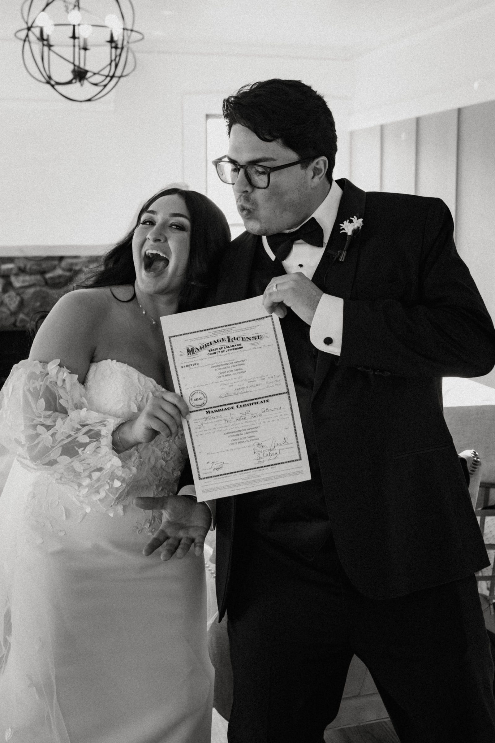 Black and white photo of a laughing bride and groom holding up their marriage license