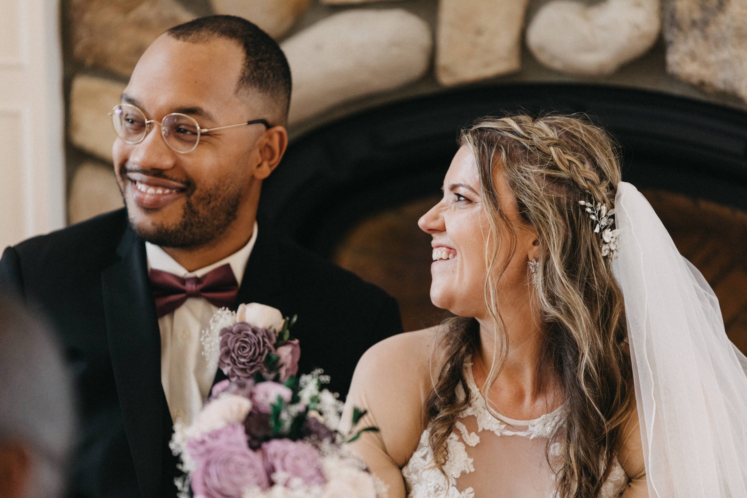 Close-up of a smiling bride and groom in front of a stone fireplace
