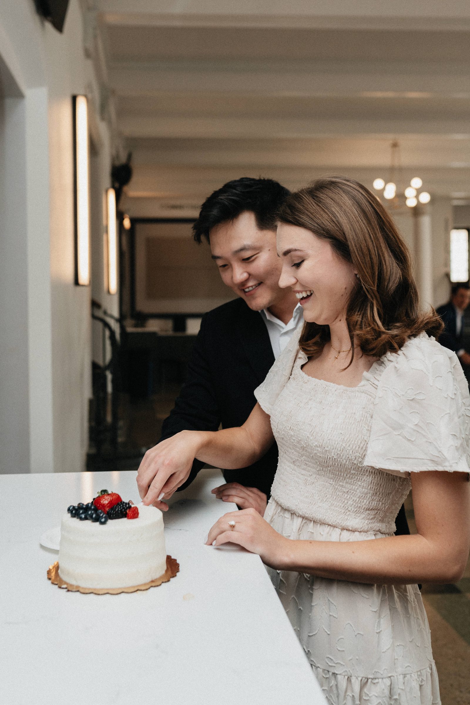 Couple laughing as they cut a small cake topped with fresh berries