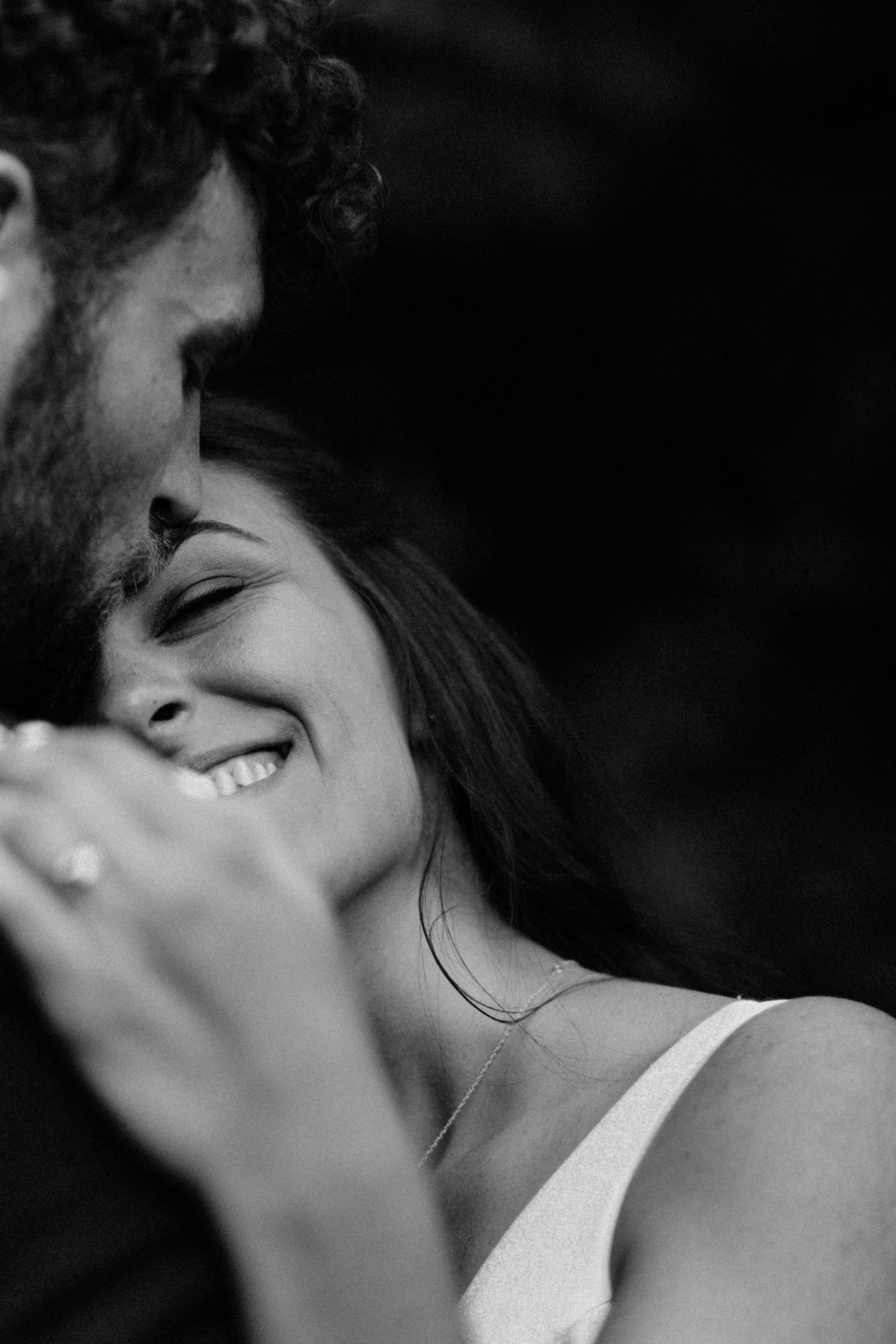 Black and white close-up of a laughing bride resting against her groom's shoulder