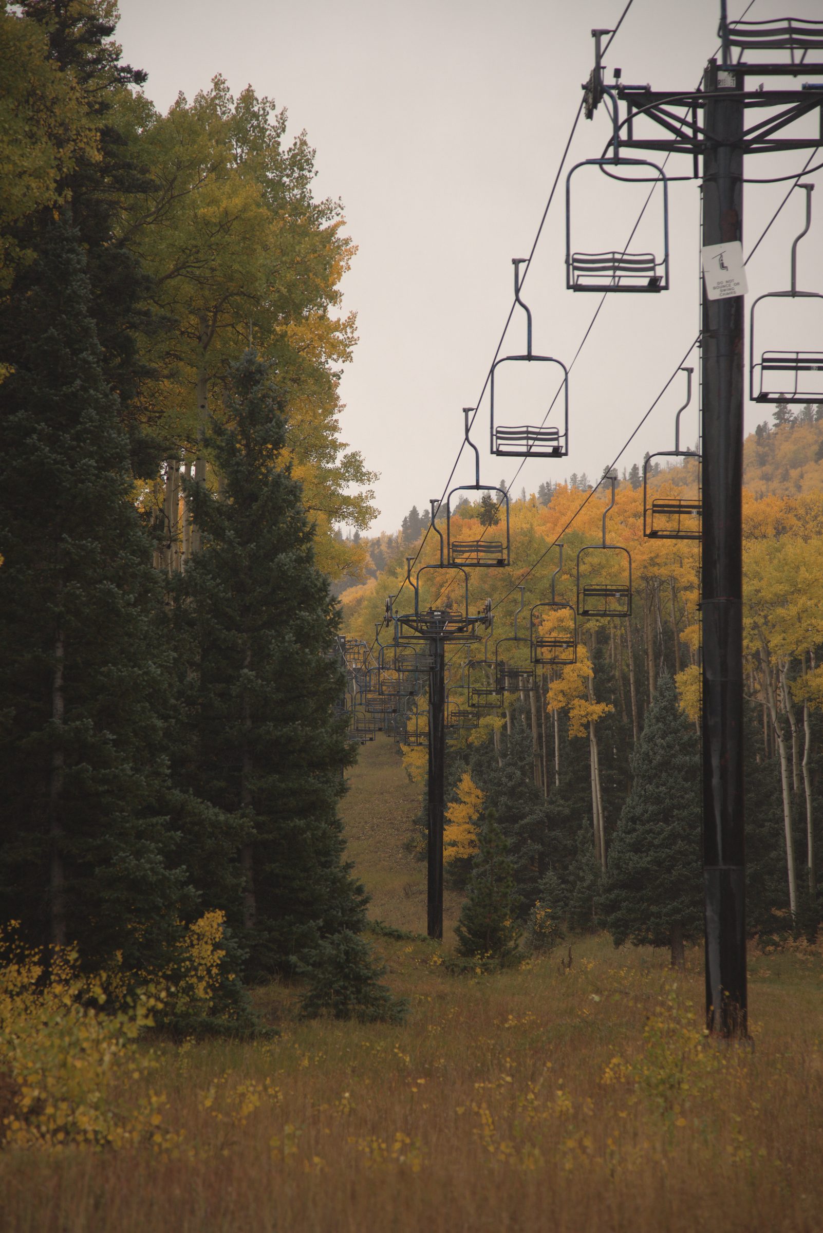 Empty chairlift hanging above golden aspens and evergreens on a misty autumn mountainside